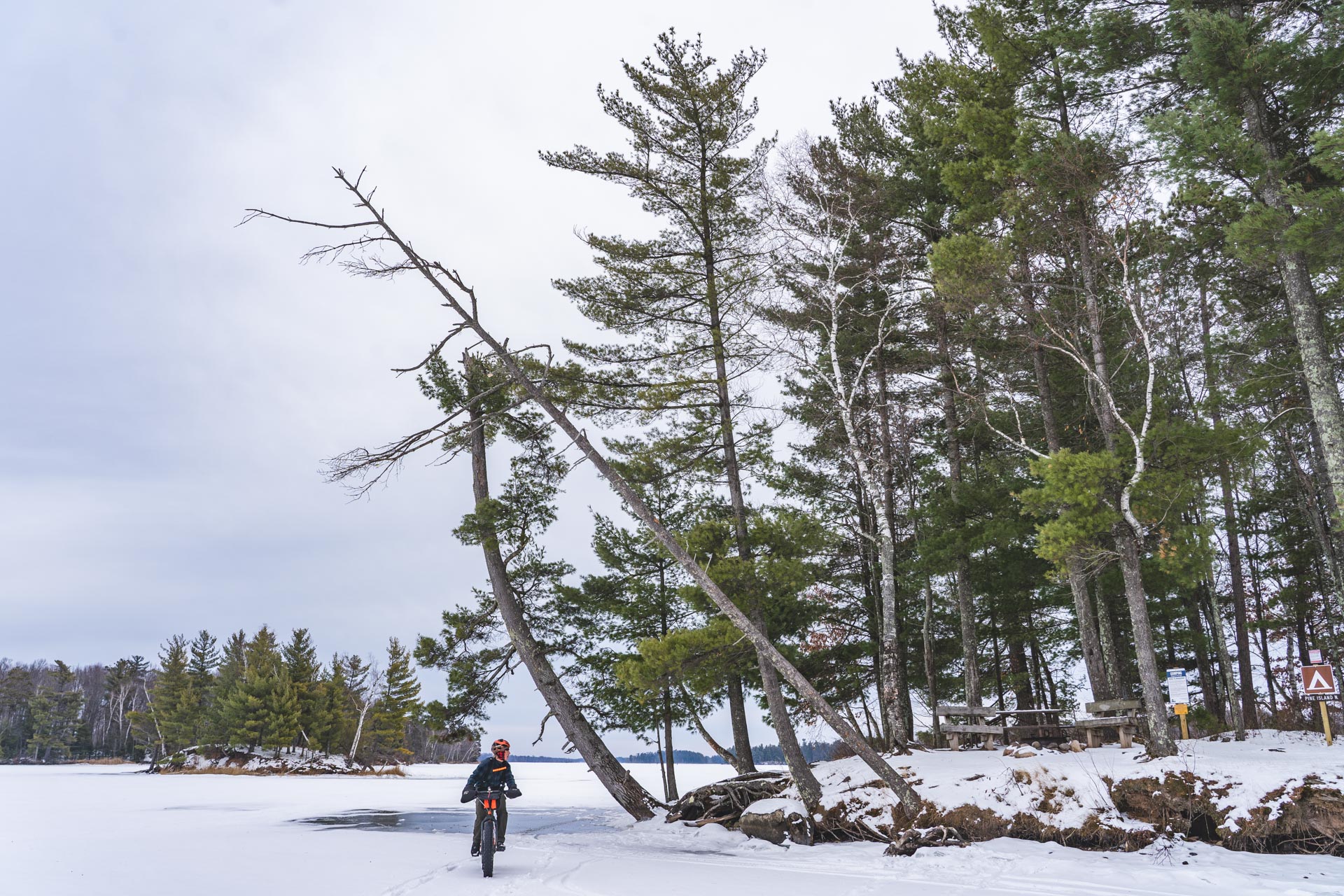 Man riding fat bike on frozen Chippewa Flowage past island campsite.