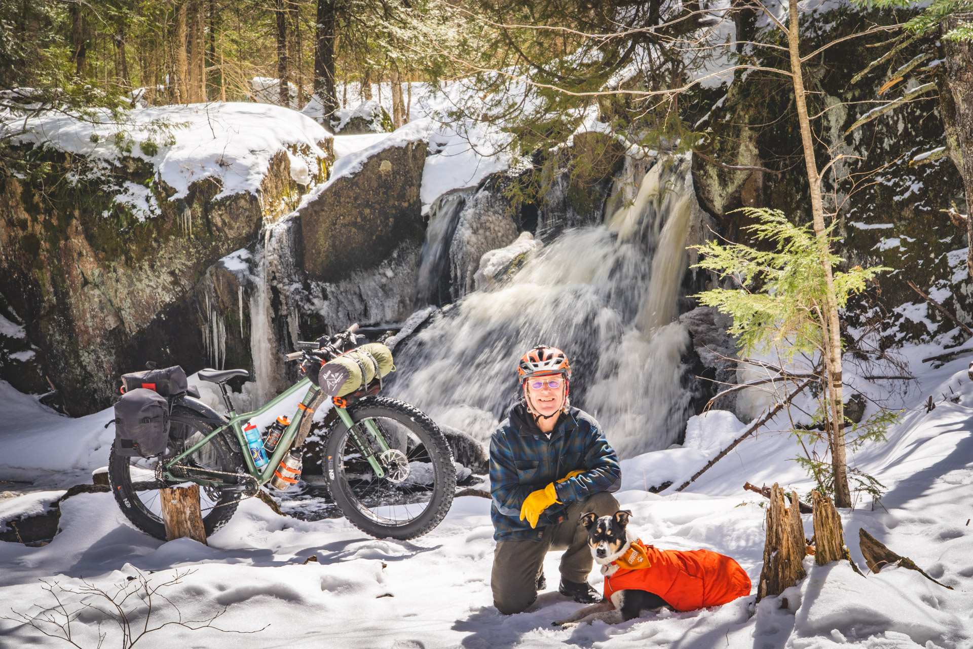Man and dog in snow next to fat bike and waterfall