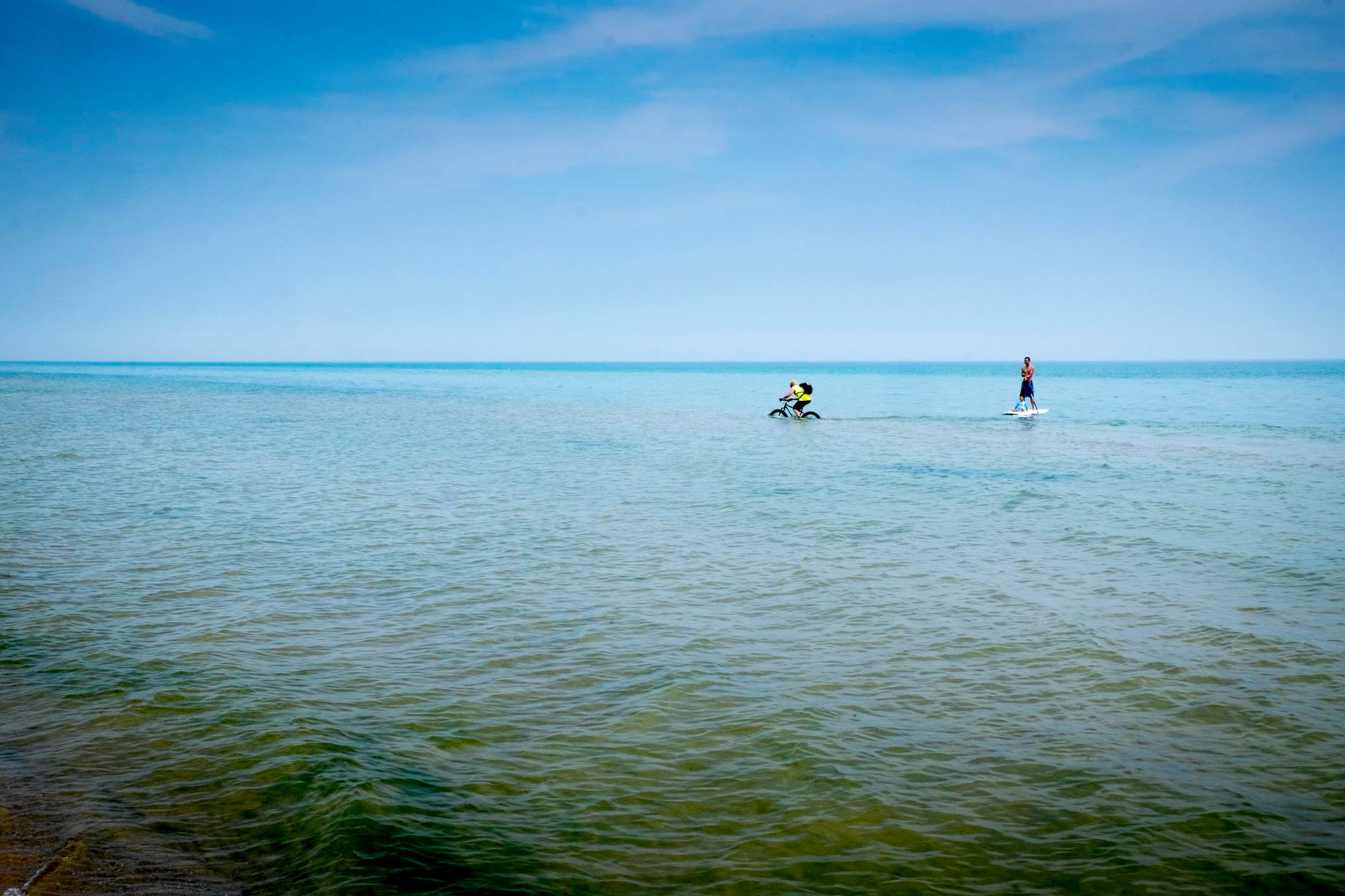 Man rides fat bike in Lake Michigan next to another man on a SUP