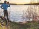 Man drinks water next to fat bike looking at sunset over lake